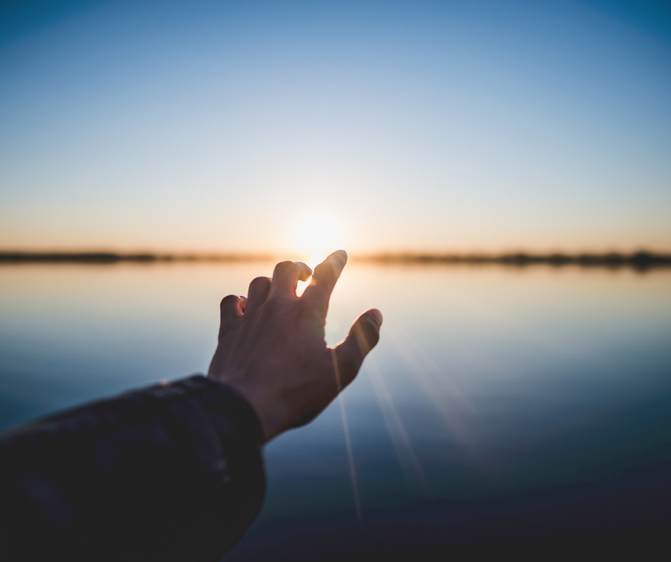 photo of a hand reaching out with optimism to a sunrise